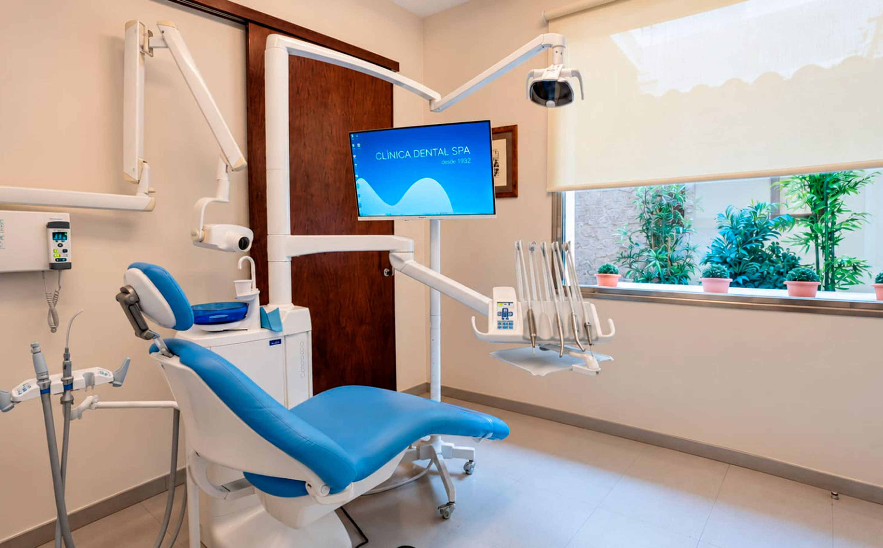 Box de tractament amb cadira dental, monitor i finestra amb plantes