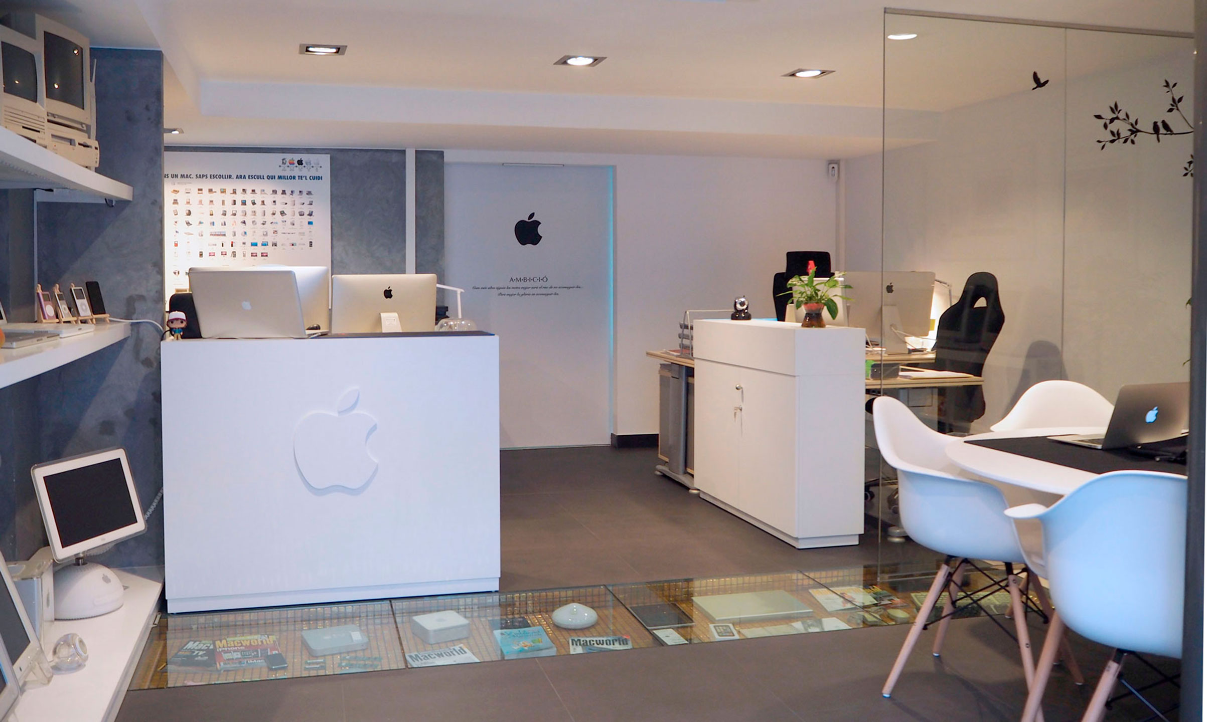 Recepció de les oficines de SimóMac, amb el taulell amb el logo d'Apple, iMacs i una vitrina de Macs clàssics al terra